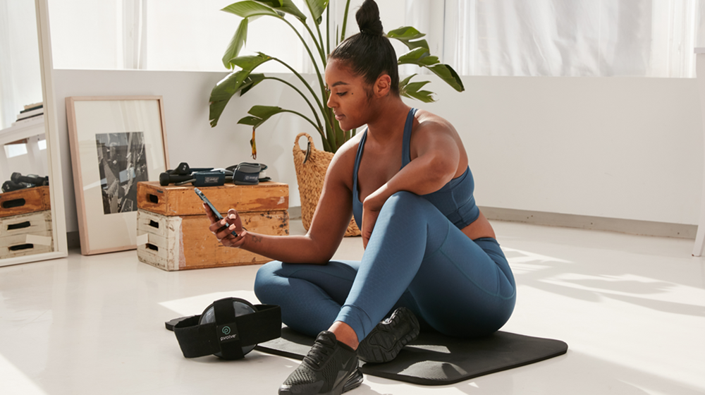 Woman sitting on a yoga mat looking at her phone inside a P.volve studio.